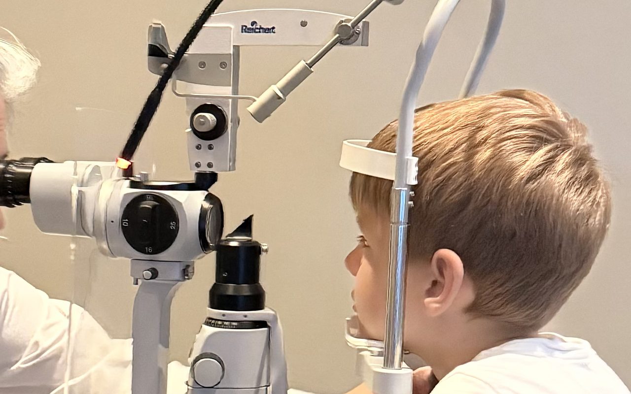 Young boy resting at the slit lamp while Dr. Roxanna Gangi examines his eyes during a children eye exam for eye rubbing and irritation
