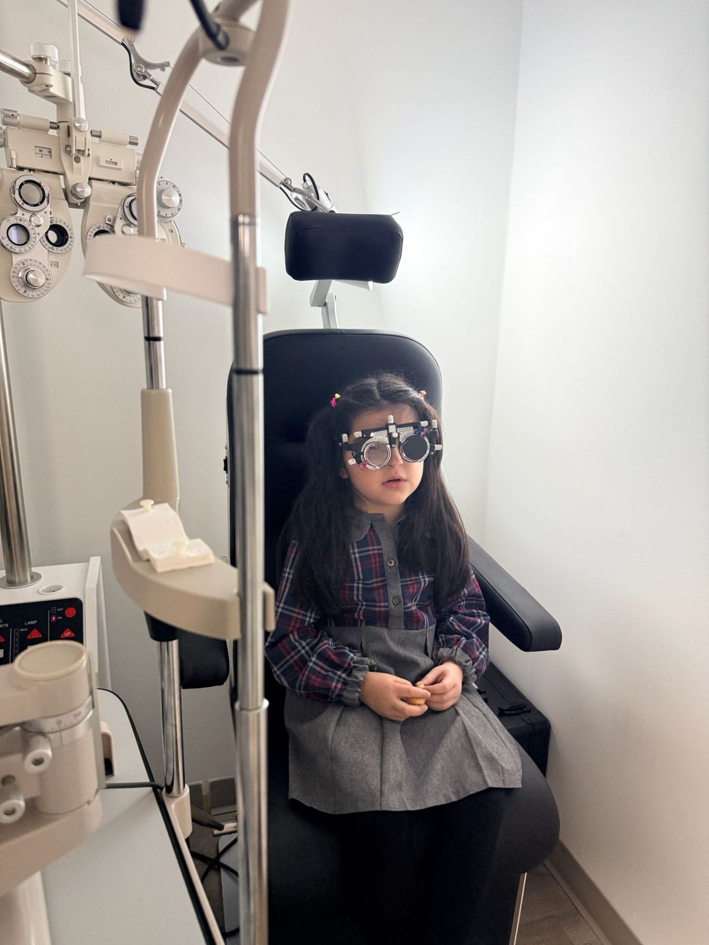 A young girl seated in an optometry exam chair wearing a trial frame during a children's eye exam with Dr. Roxanna Gangi.